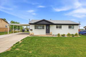 View of front facade with an attached carport, a front yard, brick siding, a shingled roof, and concrete driveway