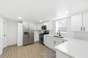 Kitchen featuring stainless steel appliances, light wood-style floors, recessed lighting, white cabinetry, and light stone counters