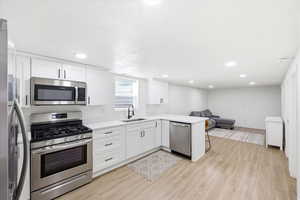 Kitchen with stainless steel appliances, a peninsula, open floor plan, light wood-style floors, and a kitchen bar