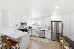 Kitchen with stainless steel appliances, white cabinets, a peninsula, a breakfast bar area, and light wood-style flooring