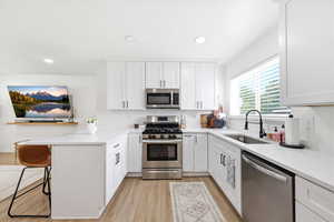 Kitchen featuring stainless steel appliances, white cabinets, light wood-style floors, a breakfast bar, and light stone countertops