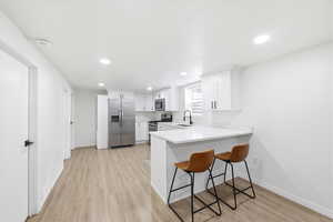 Kitchen with stainless steel appliances, a kitchen breakfast bar, a peninsula, light wood-type flooring, and white cabinets