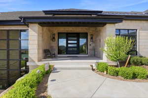 Property entrance featuring covered porch, stone siding, and a shingled roof