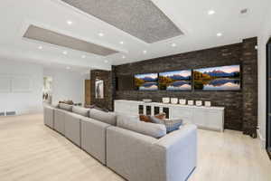 Living room featuring brick wall, light wood finished floors, recessed lighting, and a tray ceiling