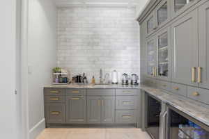 Bar featuring gray cabinets, light stone countertops, glass fronted cabinets, and beverage cooler