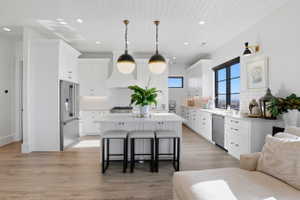 Kitchen with a kitchen bar, a center island, white cabinets, light wood-style flooring, and stainless steel appliances