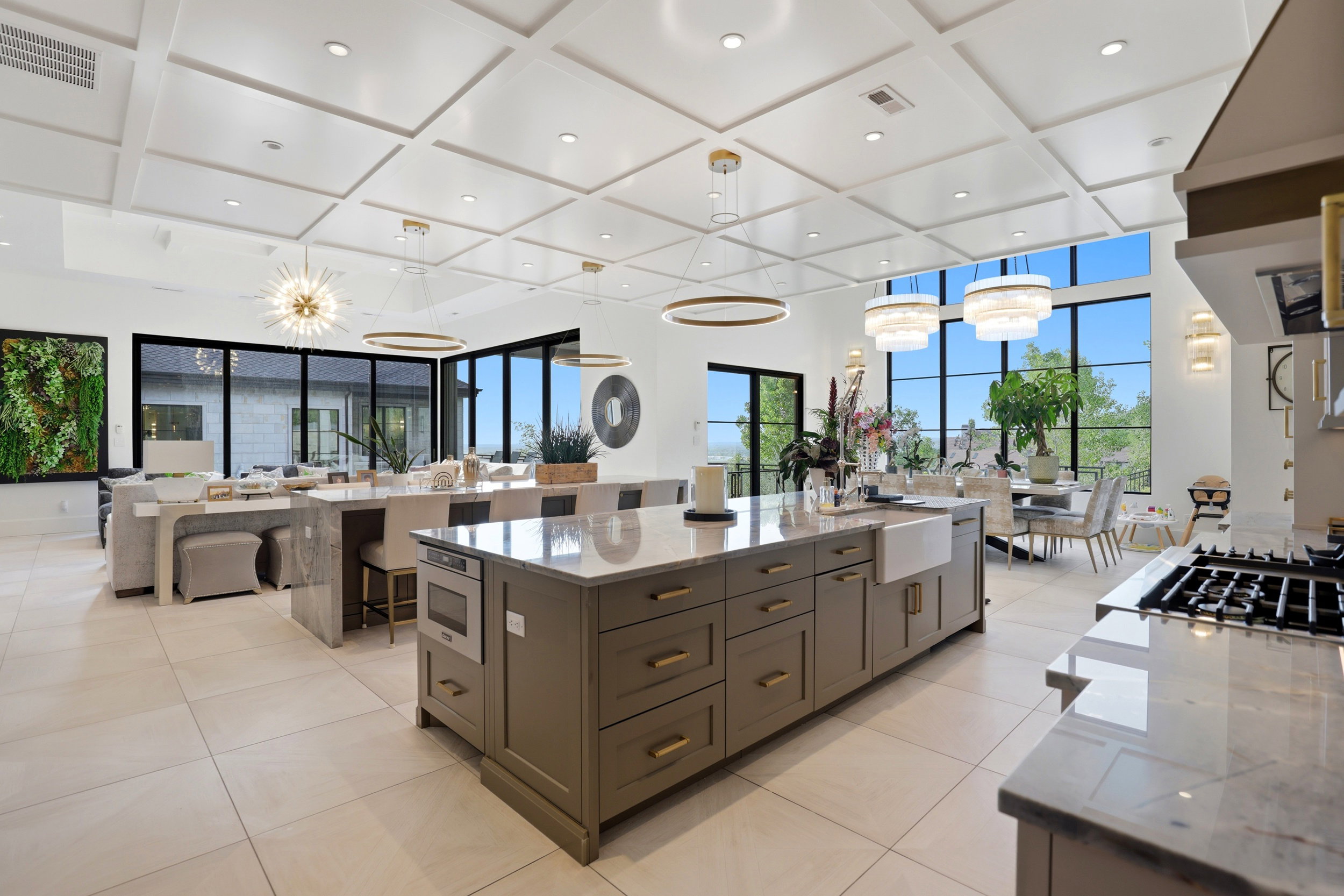 Kitchen with light stone counters, coffered ceiling, extractor fan, open floor plan, and hanging lights