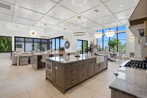 Kitchen with light stone counters, coffered ceiling, extractor fan, open floor plan, and hanging lights