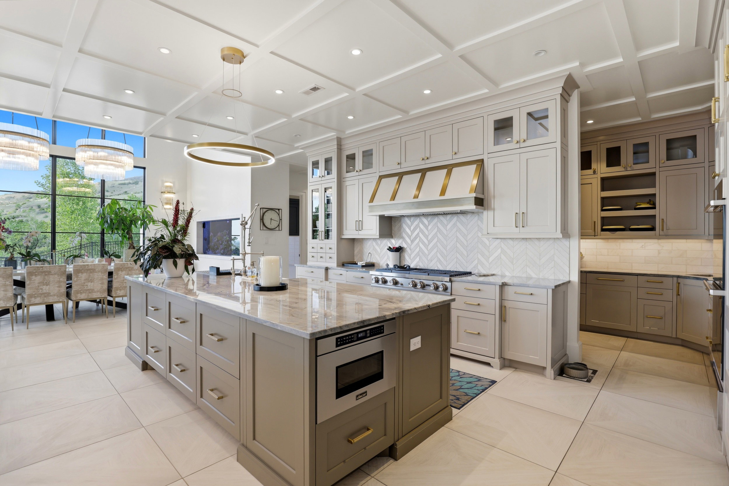 Kitchen with coffered ceiling, light stone counters, two tone color scheme, a center island, and backsplash