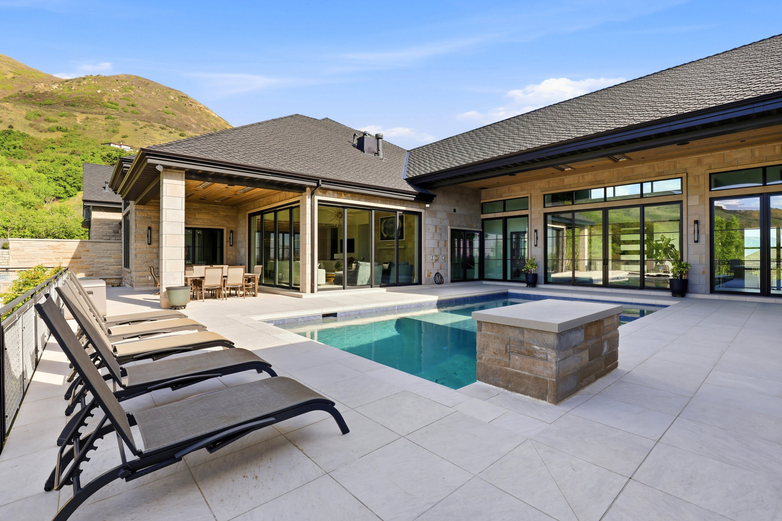 Rear view of house with outdoor dining area, an outdoor pool, stone siding, a patio area, and roof with shingles