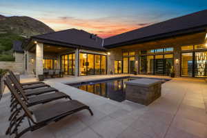Back of house at dusk featuring roof with shingles, stone siding, and outdoor dining space