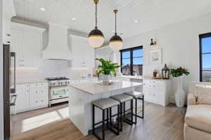 Kitchen with stainless steel appliances, white cabinets, backsplash, light wood-type flooring, and wooden ceiling