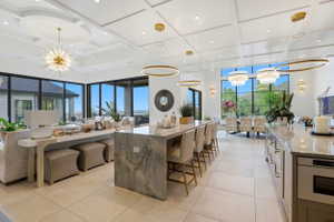 Kitchen featuring suspended lighting, coffered ceiling, light stone counters, open floor plan, and oven