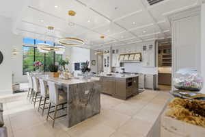 Kitchen with light stone countertops, coffered ceiling, light tile patterned flooring, hanging light fixtures, and glass insert cabinets