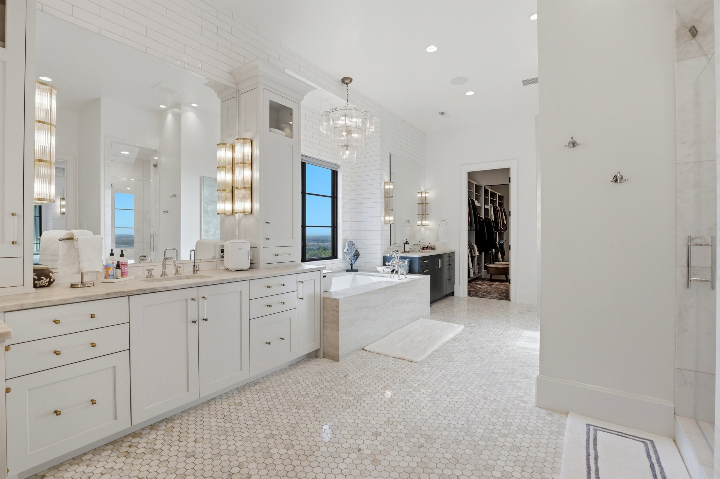 Full bath with two vanities, a walk in closet, a stall shower, a bath, and hanging lights