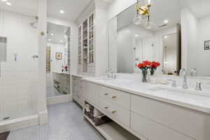 Bathroom with double vanity, a shower stall, light tile patterned floors, and recessed lighting