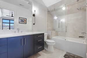 Full bath featuring vanity, tile walls, combined bath / shower with glass door, vaulted ceiling, and light tile patterned floors