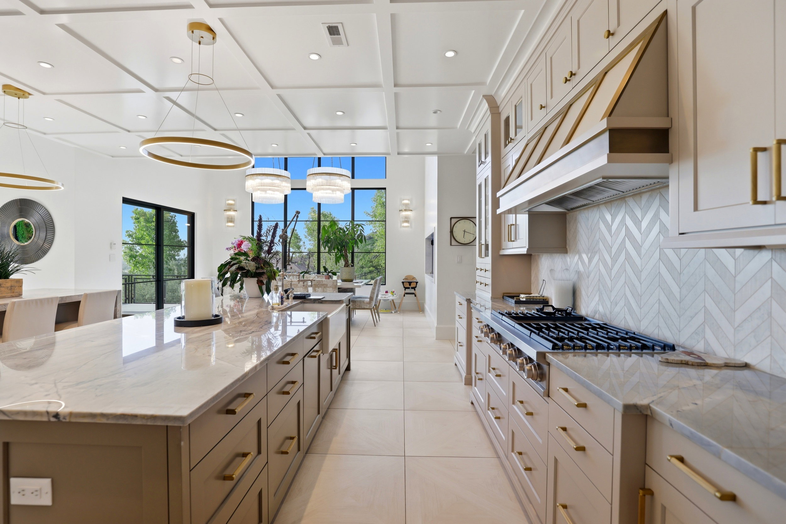 Kitchen with light stone counters, a large island, coffered ceiling, stainless steel gas stovetop, and two tone cabinetry