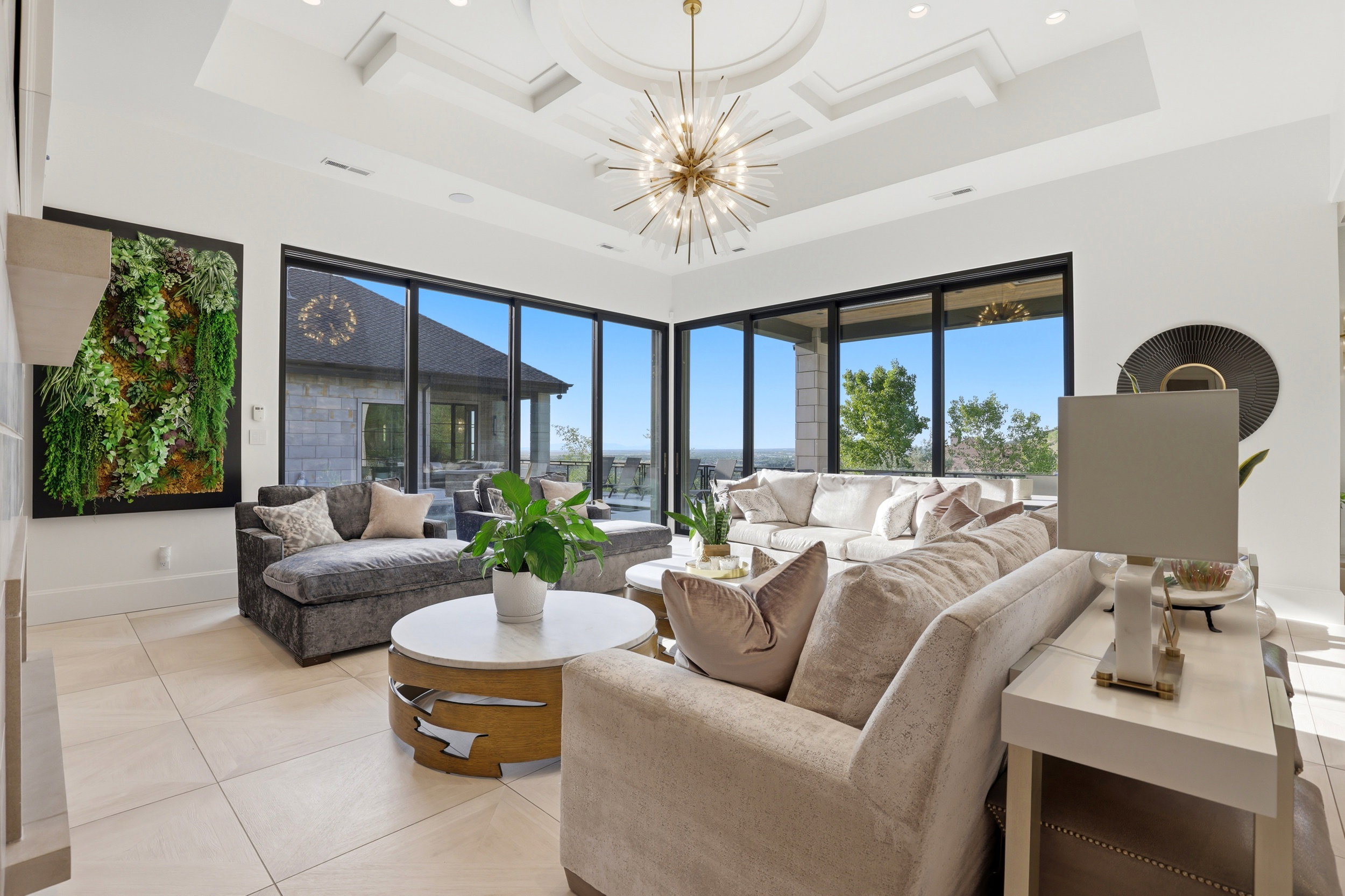 Living area with high coffered ceiling, plenty of natural light, light tile patterned floors, and a chandelier
