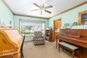 Living area with light colored carpet, a ceiling fan, and ornamental molding
