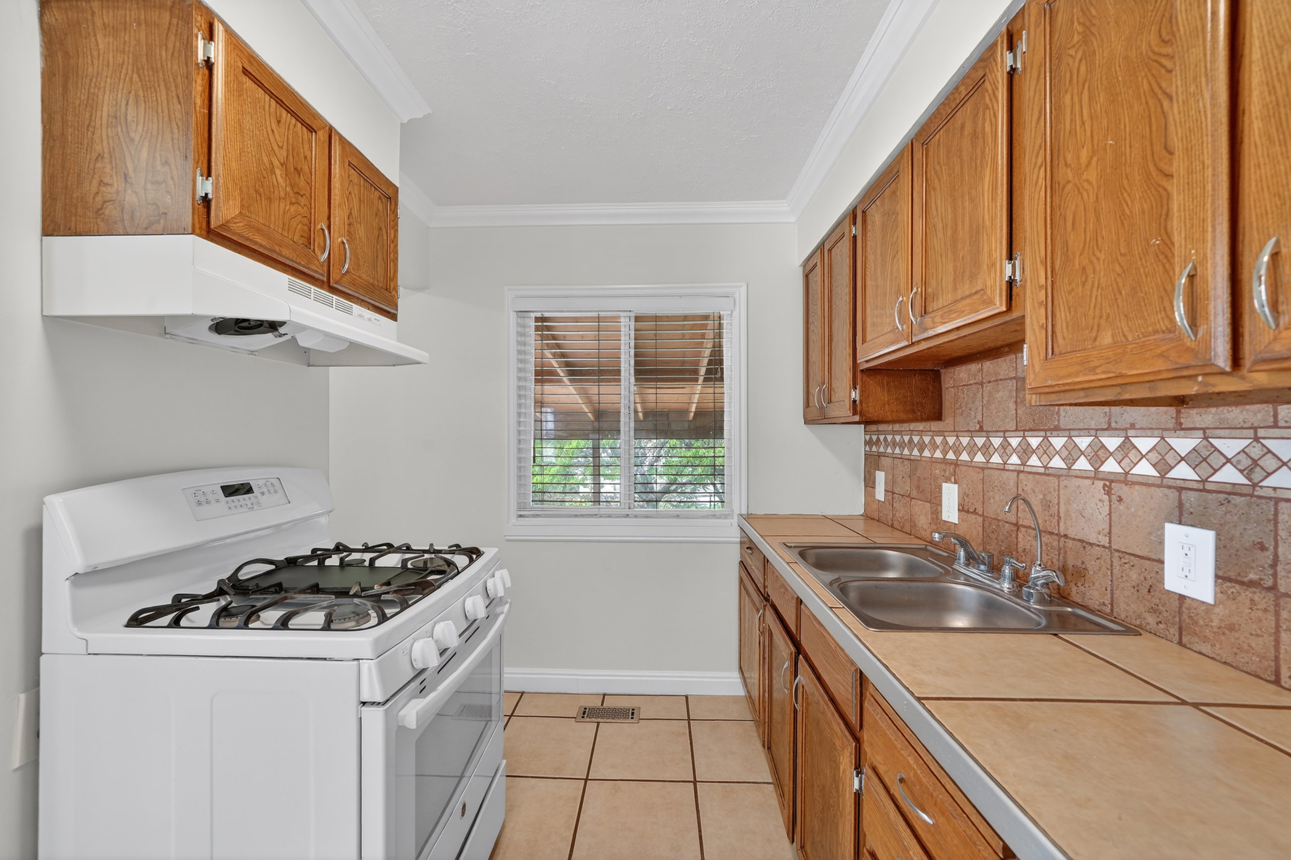 Kitchen featuring white gas stove, crown molding, tile counters, wood finish cabinetry, and light tile patterned floors