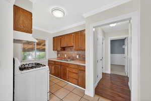 Kitchen with wood finish cabinetry, white gas stove, light countertops, light wood-type flooring, and ornamental molding