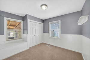 Unfurnished bedroom with carpet, a closet, a textured ceiling, and a wainscoted wall