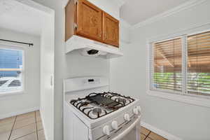 Kitchen featuring white gas range, light tile patterned floors, wood finish cabinetry, light countertops, and crown molding
