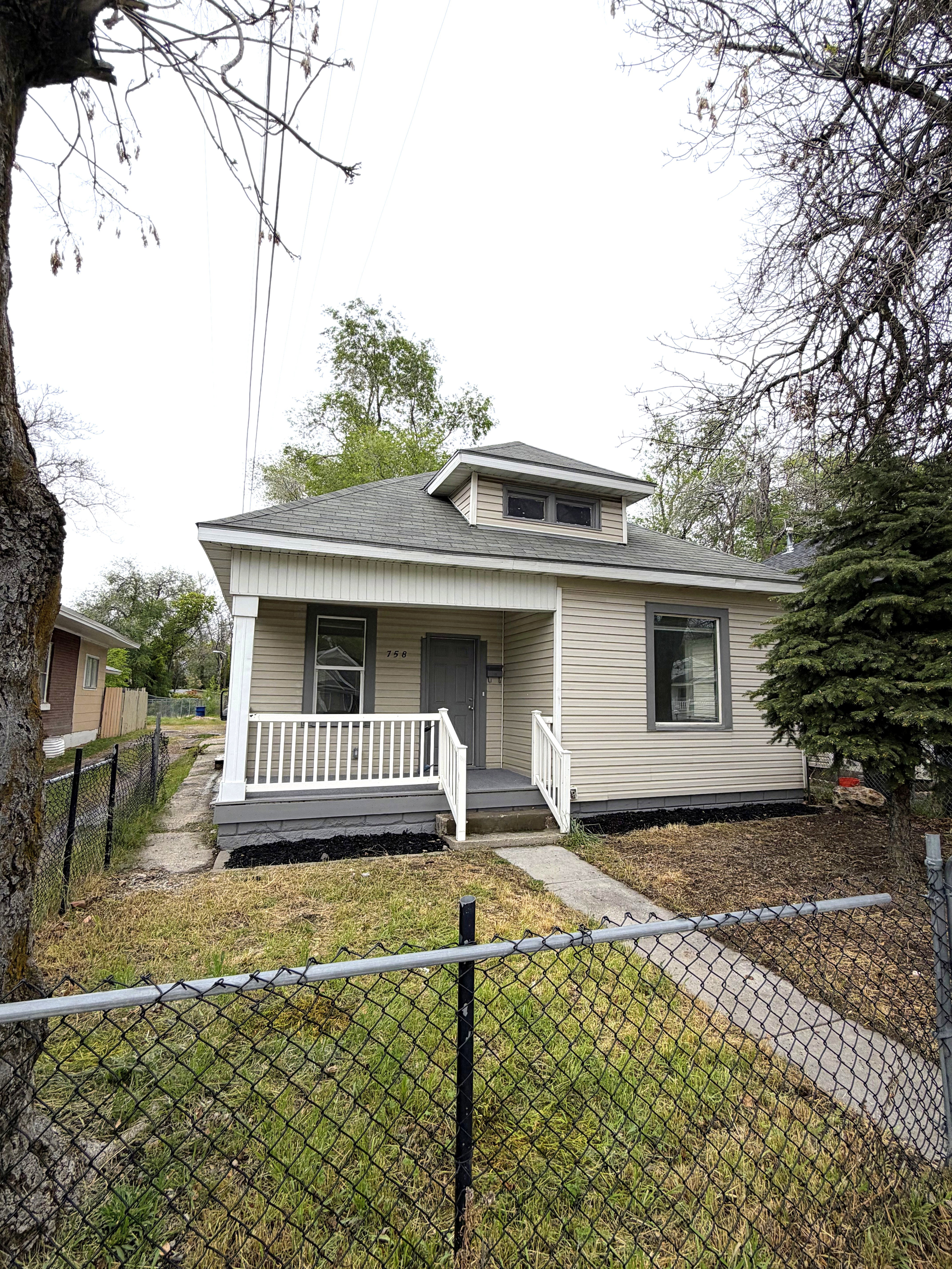 Bungalow-style home featuring a porch, a fenced front yard, and a shingled roof