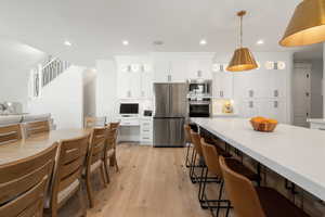 Kitchen with white cabinets, stainless steel appliances, a breakfast bar, and light wood-style floors