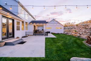 Back of house at dusk with a patio area, a lawn, and french doors