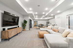 Living area with a tray ceiling, recessed lighting, and light colored carpet