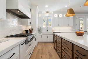 Kitchen featuring dual tone cabinetry, light wood finished floors, light stone counters, stainless steel gas cooktop, and hanging light fixtures