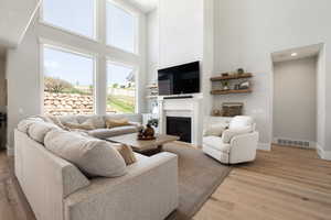 Living area featuring a high ceiling, light wood-type flooring, and a glass covered fireplace
