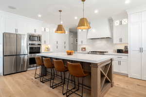 Two tone kitchen featuring stainless steel appliances, a center island, glass insert cabinets, two tone cabinetry, and a kitchen breakfast bar