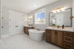 Full bath with two vanities, light marble finish floors, a freestanding tub, and walk in shower