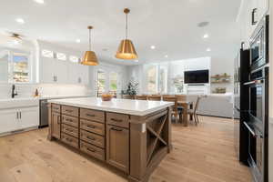 Two tone kitchen with dual tone cabinetry, a kitchen island, open floor plan, light wood-style flooring, and hanging light fixtures