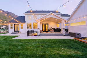 Back of property at dusk featuring french doors, a yard, a patio, and roof with shingles