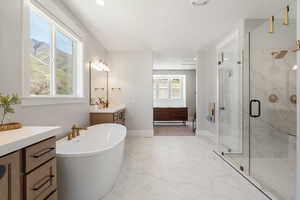 Full bathroom featuring vanity, light marble finish flooring, a marble finish shower, a freestanding bath, and recessed lighting