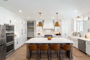 Two tone kitchen featuring a center island, stainless steel appliances, a kitchen breakfast bar, decorative light fixtures, and light wood finished floors