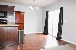 Kitchen with dark wood finish cabinets, black appliances, light countertops, an island with a sink, and dark wood-type flooring
