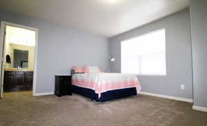 Carpeted bedroom with an ensuite bathroom and baseboards