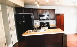 Kitchen with dark wood finish cabinets, black appliances, light countertops, an island with a sink, and dark wood-type flooring