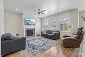 Living room with light wood-style flooring, a tiled fireplace, a ceiling fan, and recessed lighting