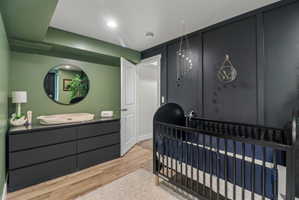 Bedroom with light wood finished floors, a nursery area, and recessed lighting