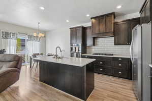 Kitchen with stainless steel appliances, open floor plan, dark wood finish cabinets, light stone countertops, and suspended lighting