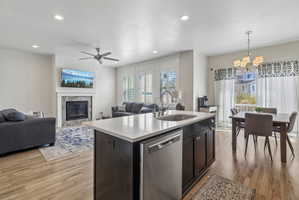 Kitchen with open floor plan, a kitchen island with sink, dishwasher, light wood-type flooring, and a high end fireplace