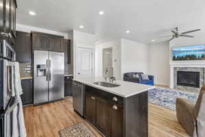 Kitchen with open floor plan, stainless steel appliances, dark wood finish cabinets, a center island with sink, and light wood-style floors