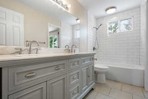 Bathroom featuring double vanity, plenty of natural light, light tile patterned flooring, and bathing tub / shower combination