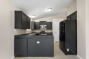 Kitchen featuring stainless steel appliances, dark cabinets, vaulted ceiling, a peninsula, and light tile patterned flooring